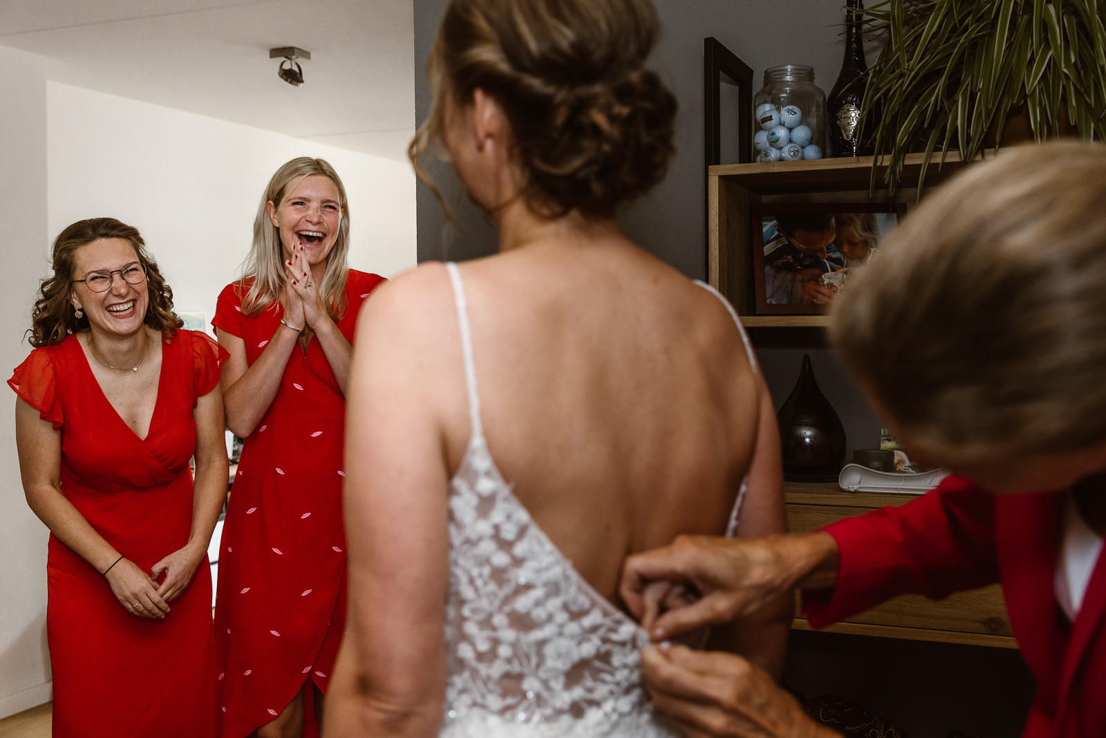 Familie kijkt hoe de trouwjurk bij de bruid wordt aangetrokken