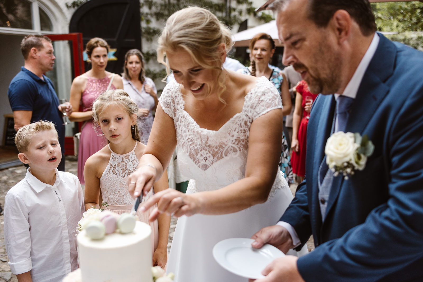 Taart wordt aangesneden door bruidspaar. Kinderen kijken toe